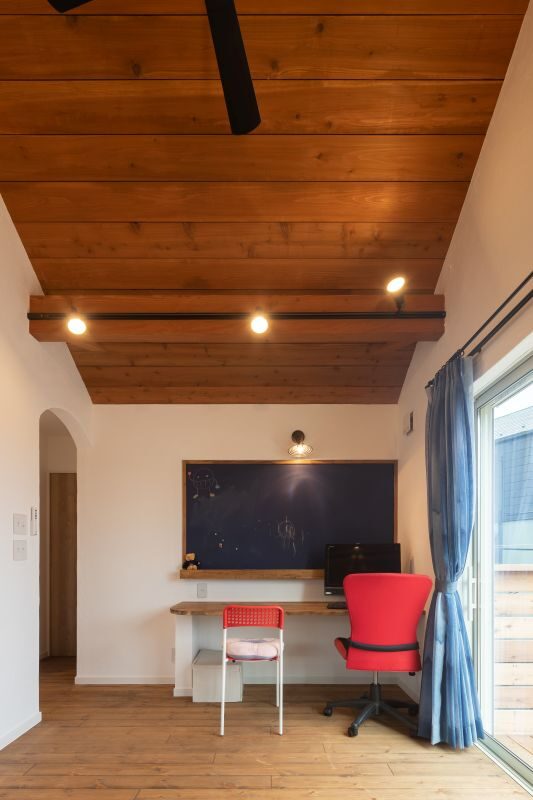 Home office corner with a chalkboard, wooden desk, and red rolling chair beneath a wooden beam ceiling.