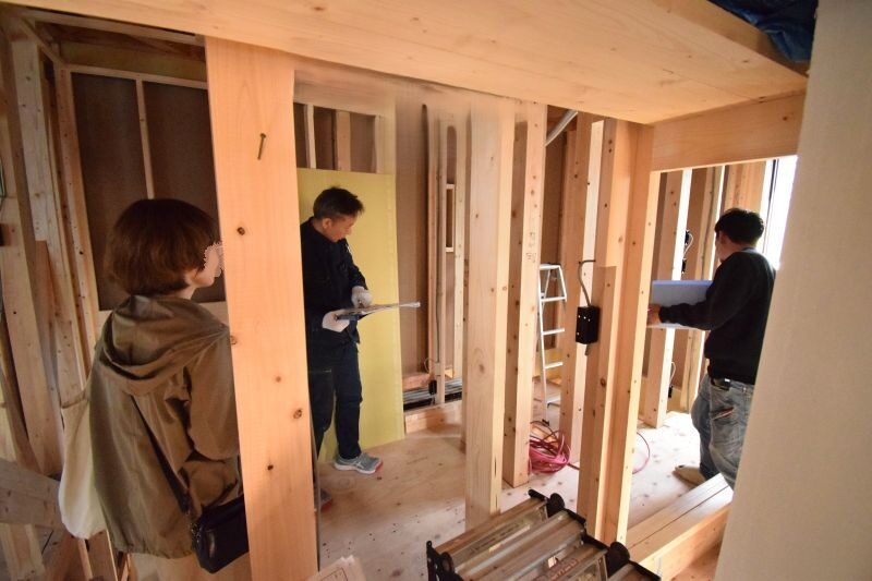 Construction site: three workers examine the wooden framing inside a partially built house.