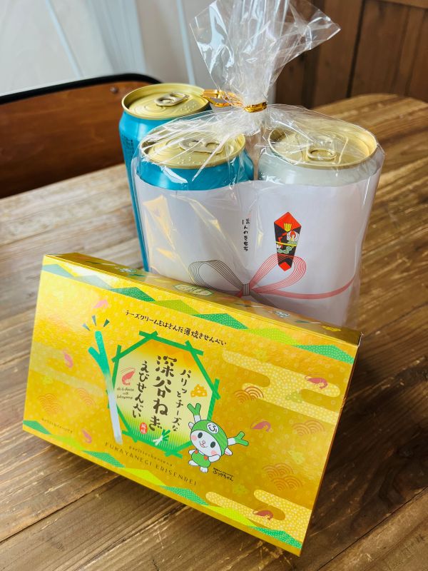 Colorful gift box with a cartoon rabbit and Japanese text, placed on a wooden table beside wrapped cans in a clear bag.