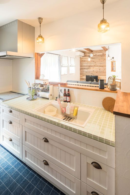 Bright white kitchen with a pale green tiled counter, double sink, and a pass-through window to a wood-paneled living area