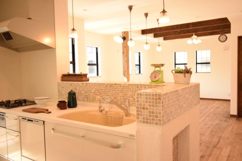 Open-plan kitchen with mosaic-tile island, beige sink, gas stove, and multiple pendant lights in a bright room.