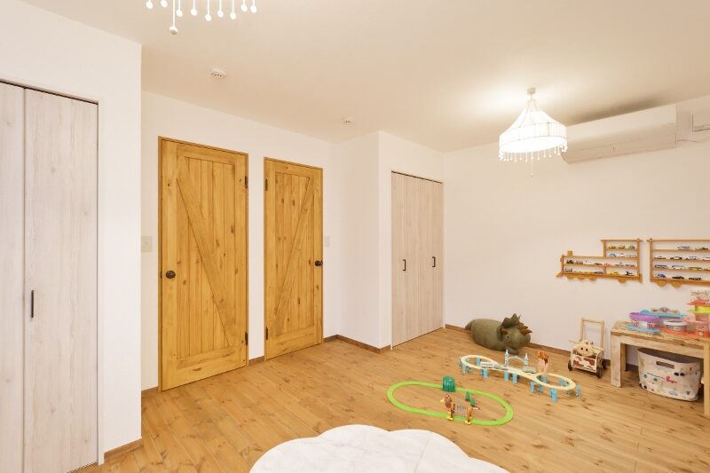 Bright playroom with white walls, warm wooden floors, and multiple doors; a toy area with tracks and figures on the floor and shelves of tiny toys to the right
