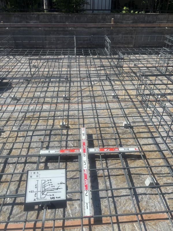 Reinforcing steel grid over a concrete surface with a red-and-white cross-shaped measurement ruler at center.