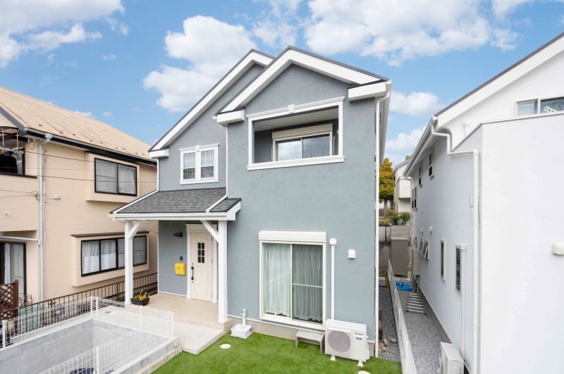 Front view of a two-story blue house with white trim, a small lawn, and a yellow mailbox by the door.
