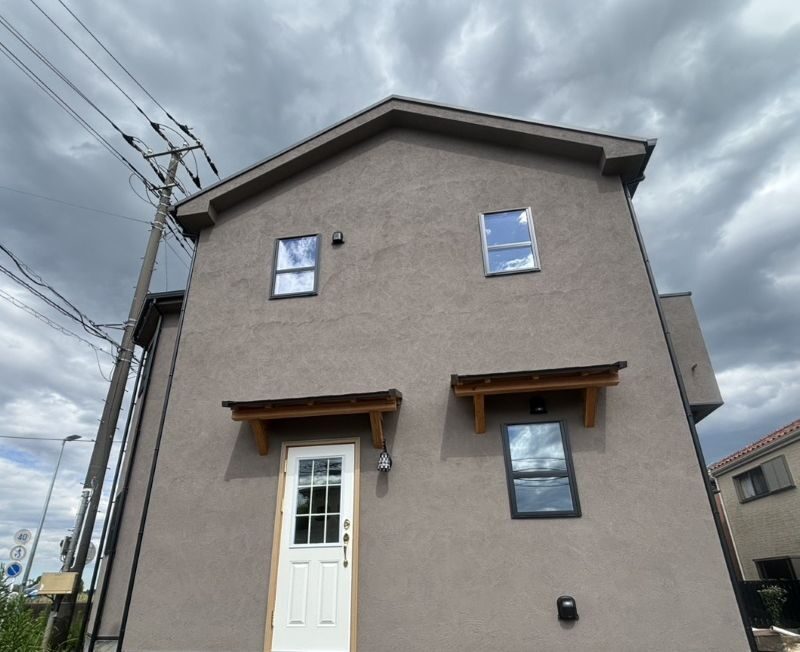 Two-story beige stucco house with a white front door under a wooden awning and cloudy sky above.