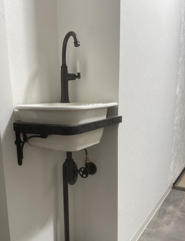 Wall-mounted utility sink with a black gooseneck faucet in a narrow corner