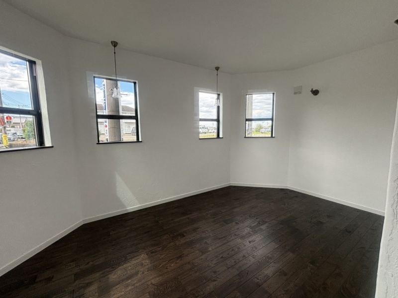 Empty white-walled room with dark wood flooring, four windows along a curved wall, and two pendant lights hanging from the ceiling.