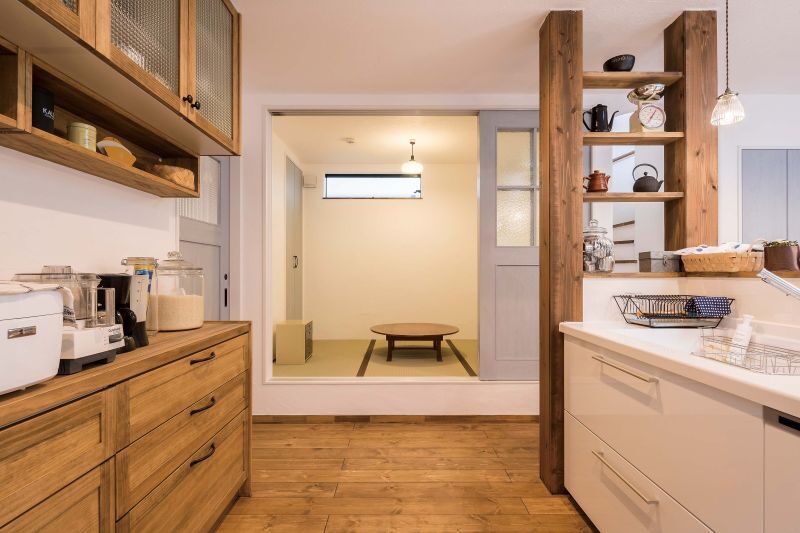 Kitchen with wooden cabinets and a doorway opening to a Japanese-style sitting area with a low round table on tatami mats.