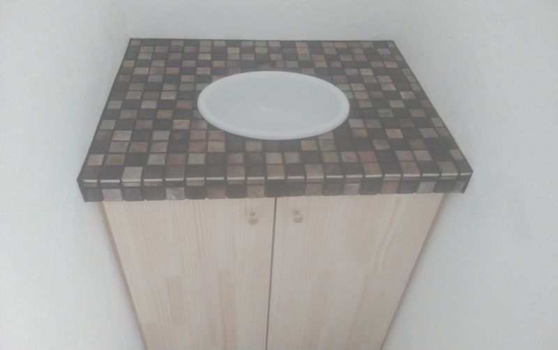 Wooden cabinet with a dark mosaic tiled countertop and a white circular plate on top in a narrow corner