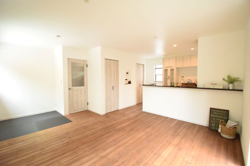 Bright open-plan living area with a kitchen island, white walls, and wood floors; entry doors and a small decor nook visible to the right goal: homey, modern space.