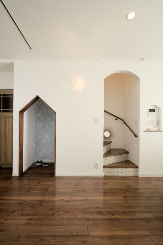 Bright, modern interior with white walls, dark hardwood floors, and a stairway arch on the right; a house-shaped doorway sits to the left.