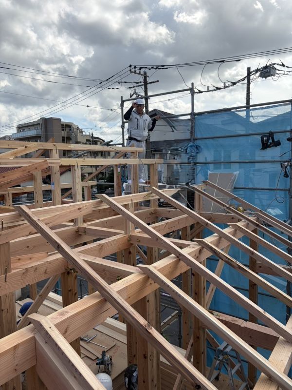 Construction worker on the upper level of a timber-framed building under construction, wearing a hard hat and safety gear, with scaffolding and cables in the background.