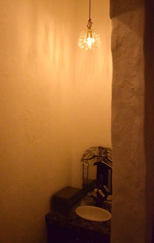 Narrow vintage bathroom with a crystal pendant light, creamy walls, an ornate mirror, and a small white sink.