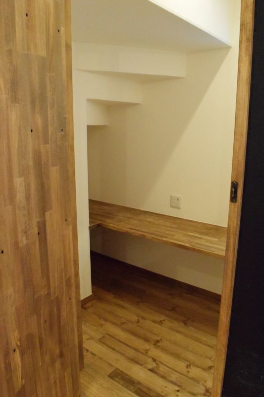 Built-in wooden desk in a stair alcove with white walls and oak flooring. Includes an electrical outlet on the wall.