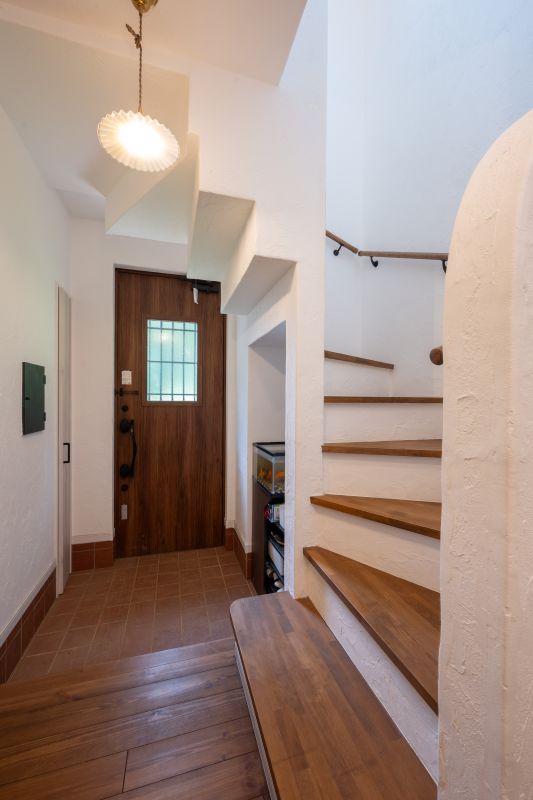Entryway featuring a wooden front door with small window, tile floor, and a curved wooden staircase on the right; a bench along the wall.